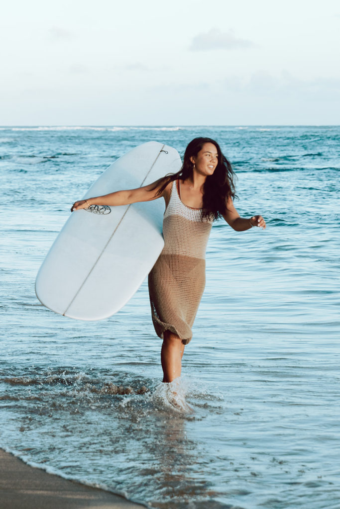 model walks through ocean with surfboard
